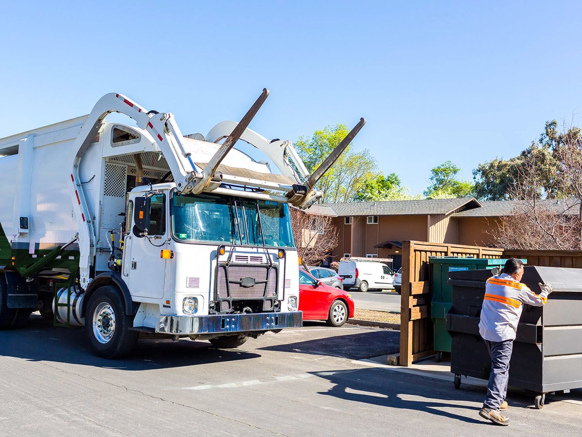 A garbage truck driver aligning a dumpster for pick up